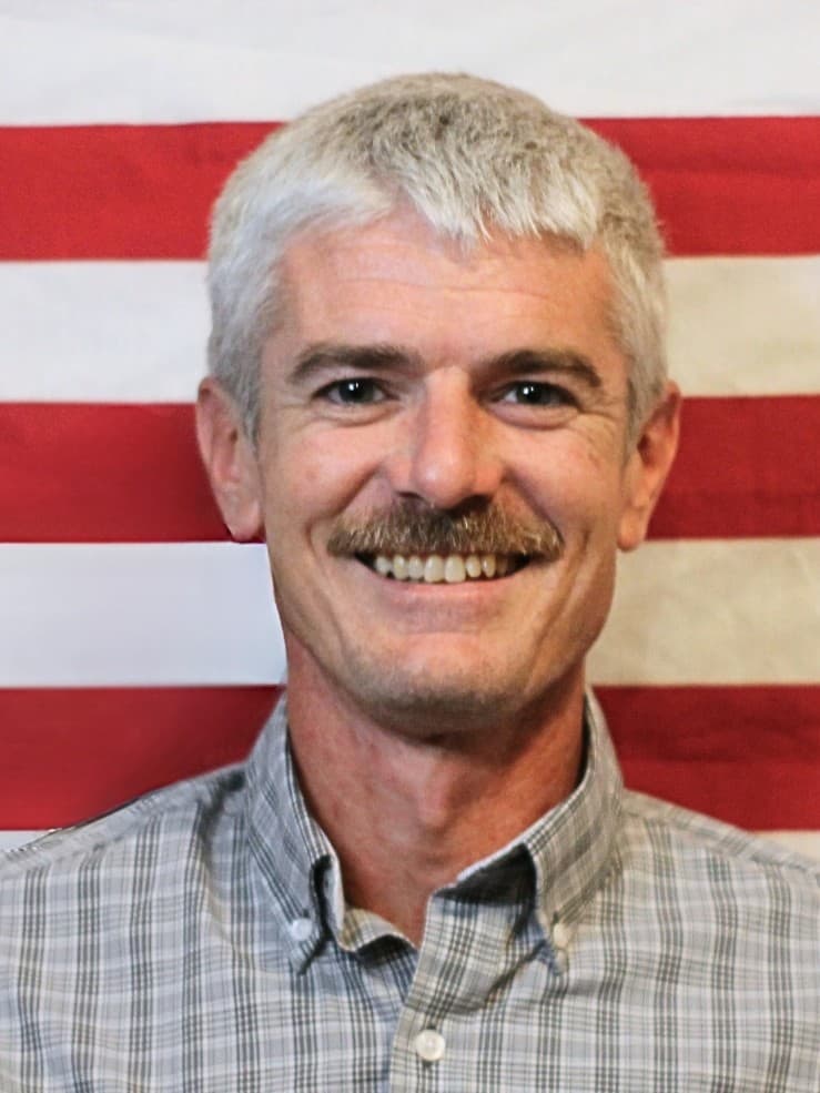 Tim Lanier smiling in front of an American flag